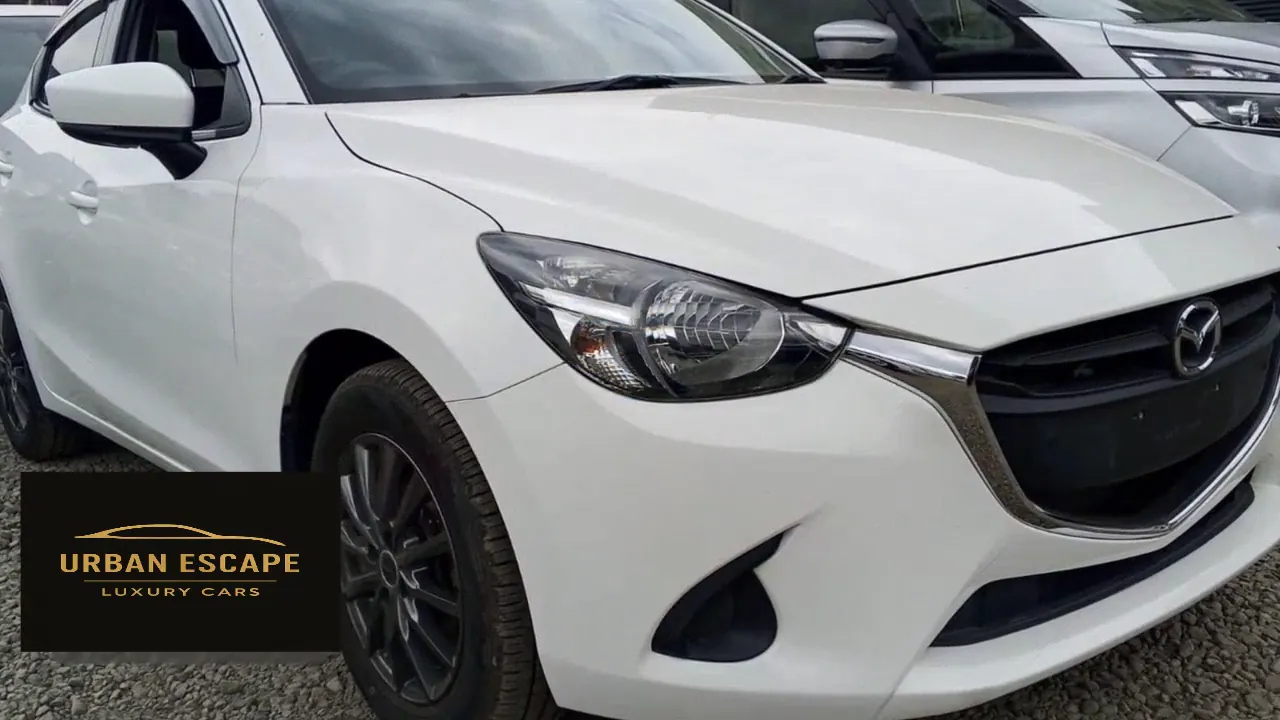 Mazda Demio in white, front three-quarter view from the right with headlight, chrome grille trim and dark alloy wheel