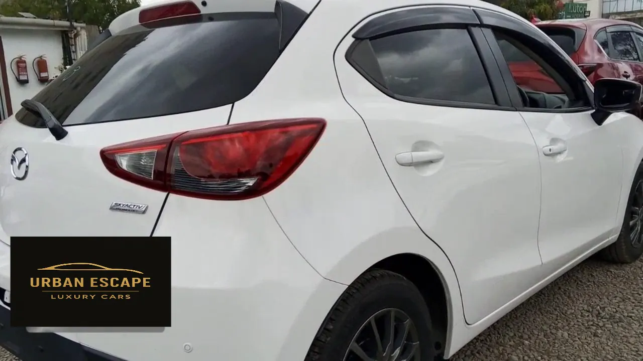 Mazda Demio in white, rear three-quarter view with red tail light, SKYACTIV badge and window deflectors
