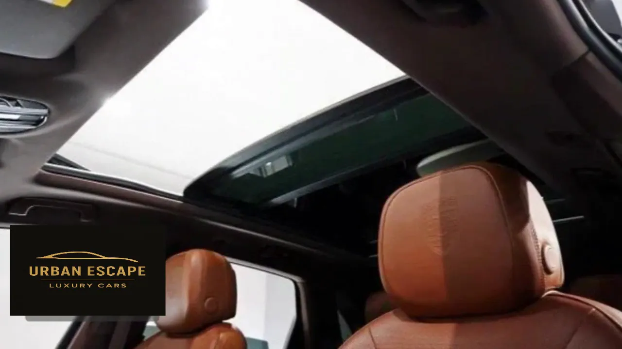 Porsche Cayenne panoramic glass sunroof above cognac leather front seats, viewed from below