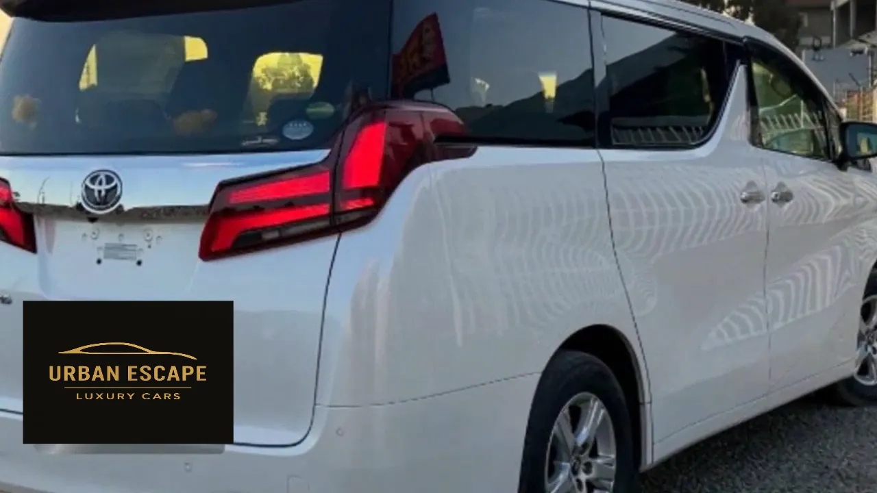 Toyota Alphard in white, rear three-quarter view showing red tail lights, side doors and silver alloy wheels