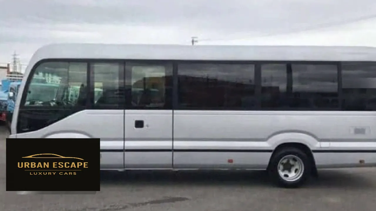 Toyota Coaster in silver, left side view showing the side door and a long row of windows
