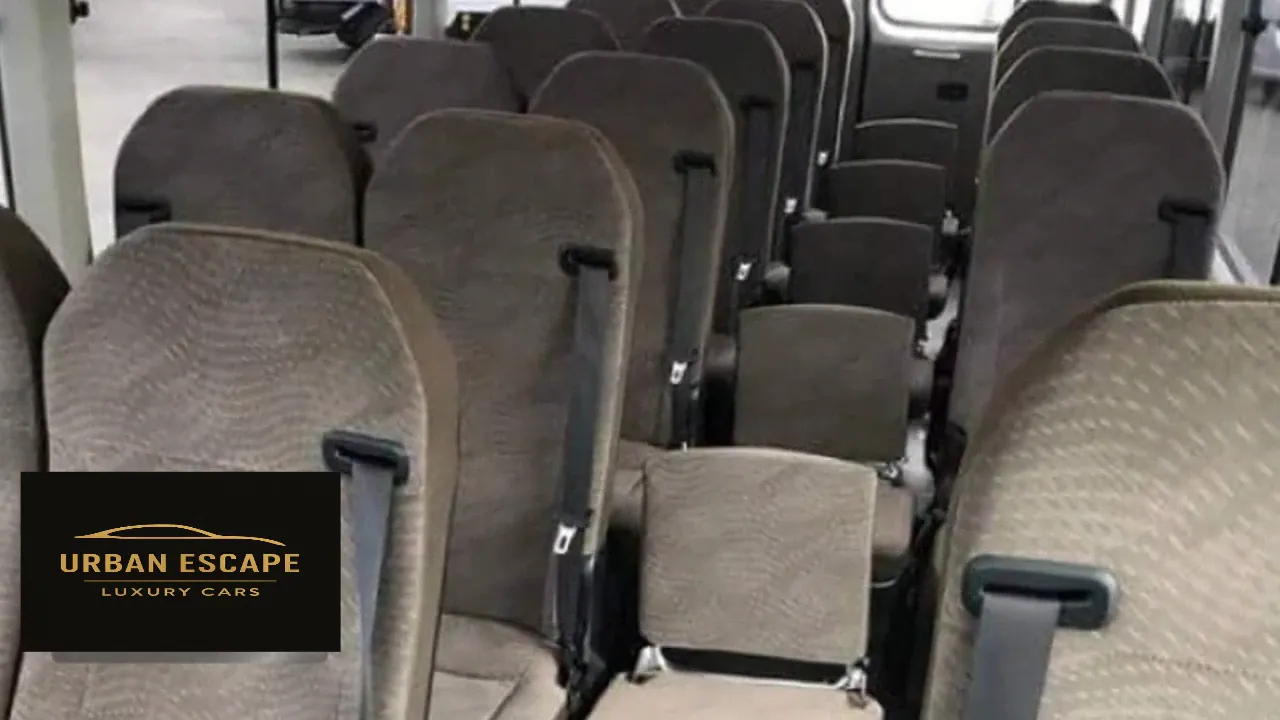 Toyota Coaster interior, rows of taupe fabric passenger seats with seat belts, including seats in the aisle
