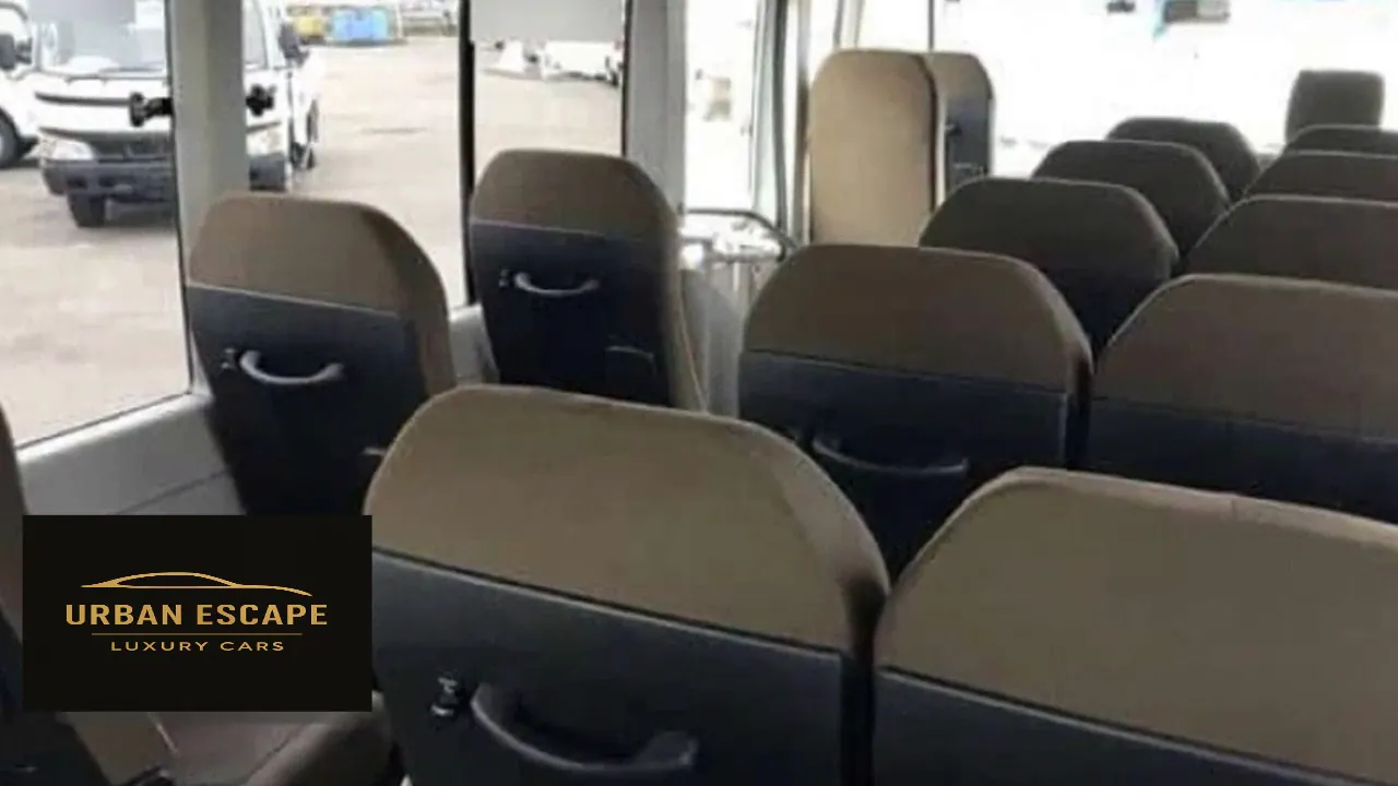 Toyota Coaster interior, view forward over rows of taupe and dark grey seats with grab handles on the backs