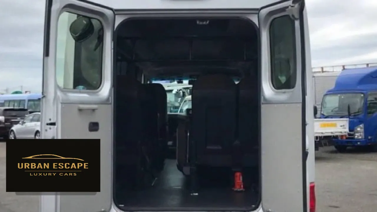 Toyota Coaster in silver with both rear doors open, showing the floor space and seats inside