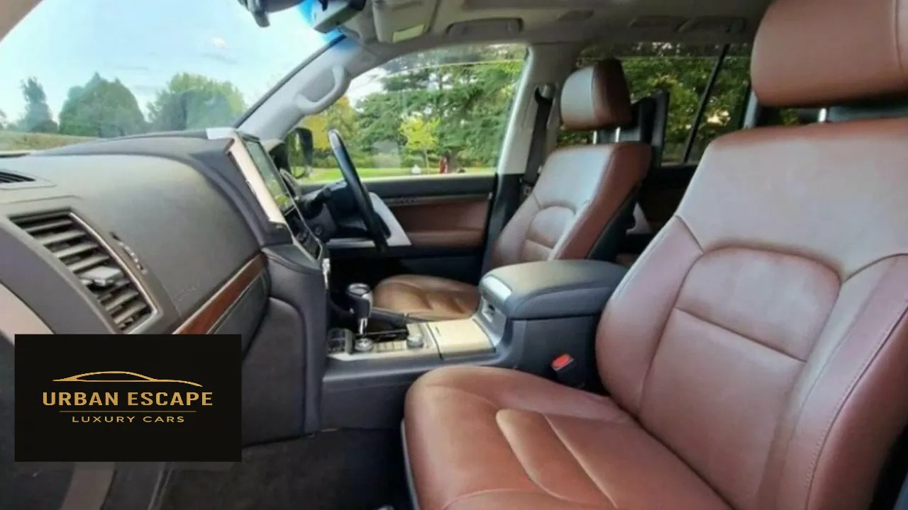 Toyota Land Cruiser V8 cabin with brown leather front seats, wood-trimmed dashboard and steering wheel