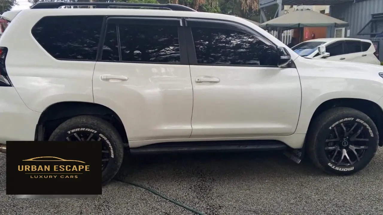 Toyota Land Cruiser Prado in white, side view with tinted windows, side steps and black alloy wheels